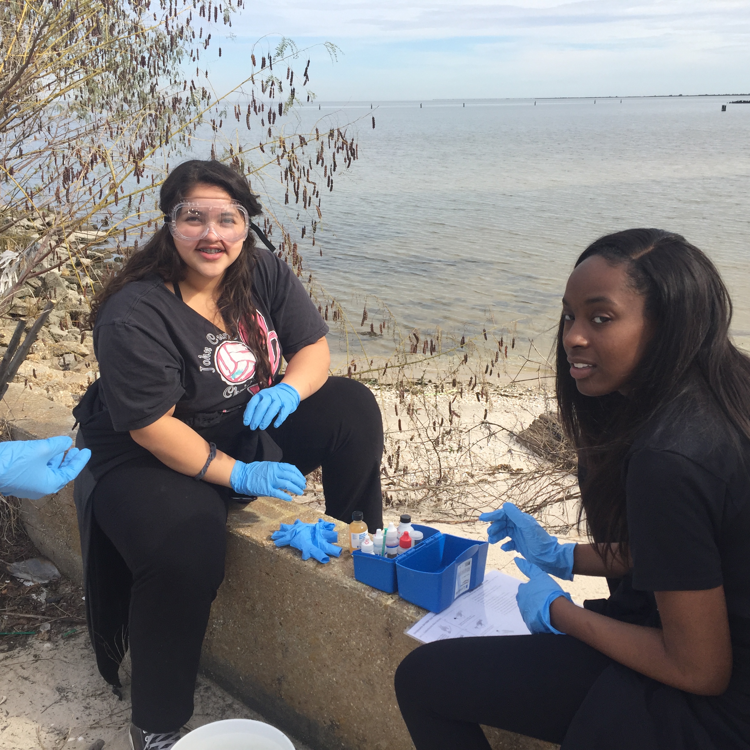 2 students sit along Lake Pontchartrain measuring dissolved oxygen