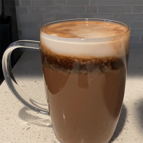 A looping GIF of a layered drink (milk on top, dark espresso in the center, and lighter hot chocolate at the bottom) being blown on. This starts to create the effect of the top two layers of milk and espresso rotating in a circle vertically: as the milk is blown to the left edge of the mug and is forced downward, the espresso on the right side is pushed up to the top of the drink. 