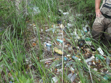 Photo of a man in a marsh filled with marine debris.