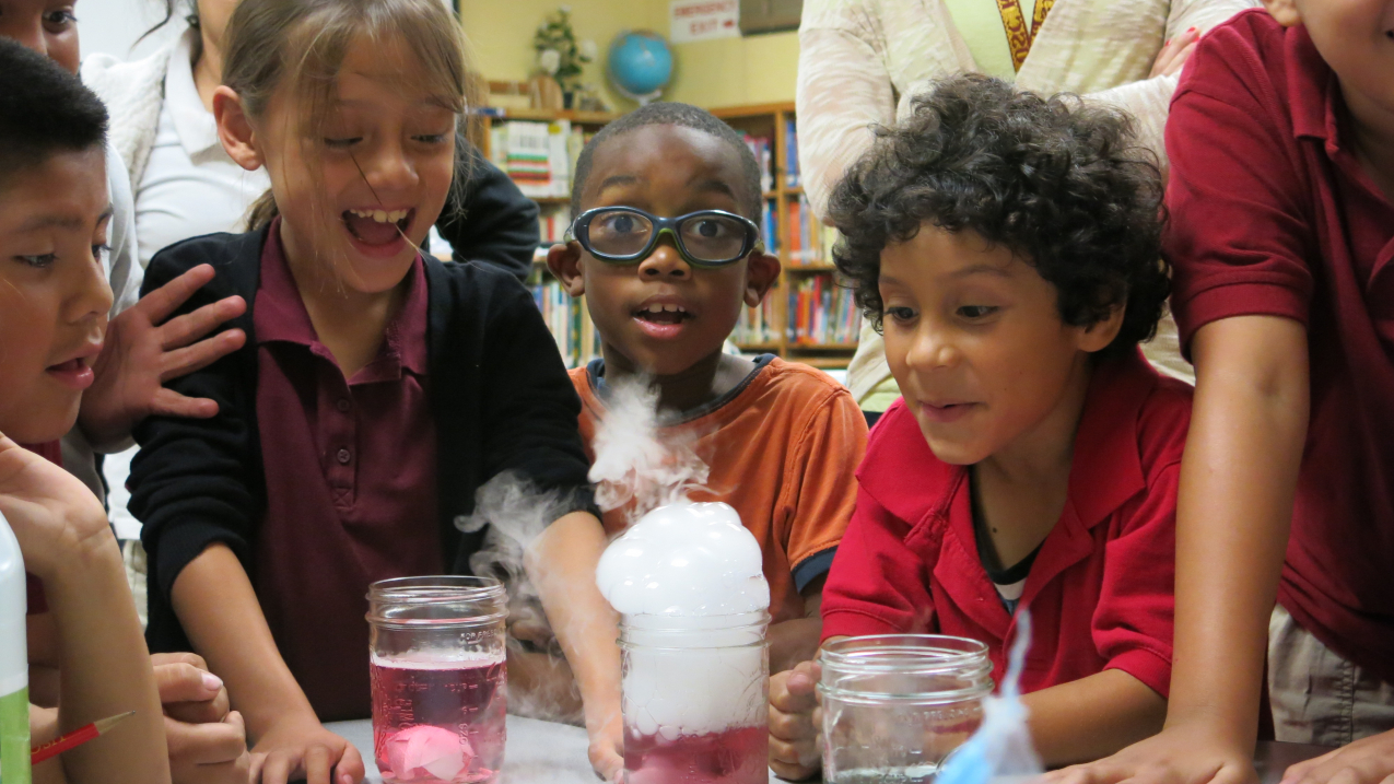 Young students gather excitedly around a chemistry experiment.
