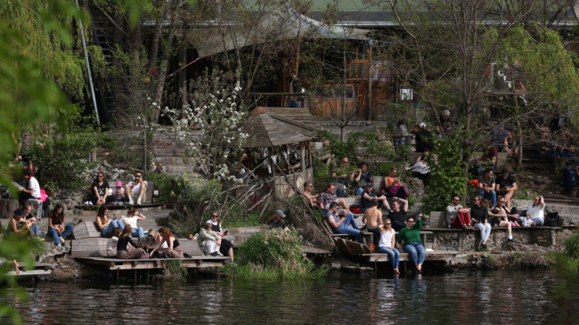 People relax at the Holzmarkt complex on the bank of the Spree River during unseasonably warm weather on April 07, 2024 in Berlin, Germany.