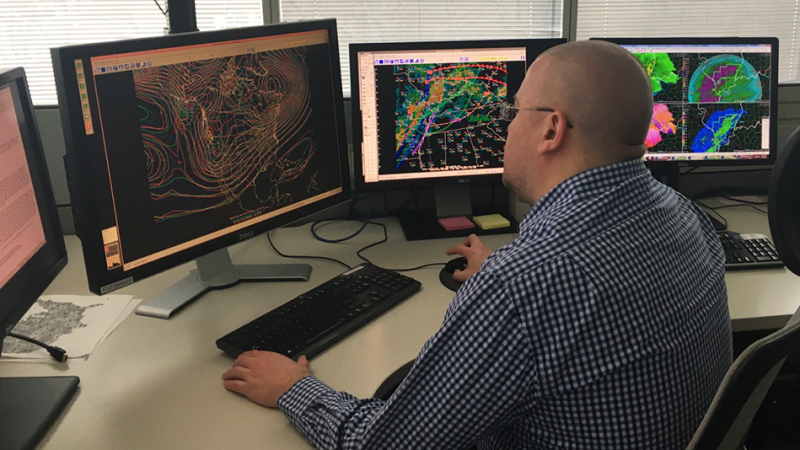 A meteorologist sits in front of several computer monitors showing different meteorological data.