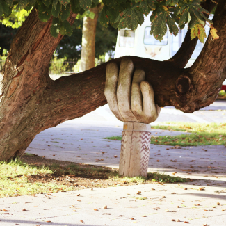 Image of leaning tree supported by a giant wooden hand