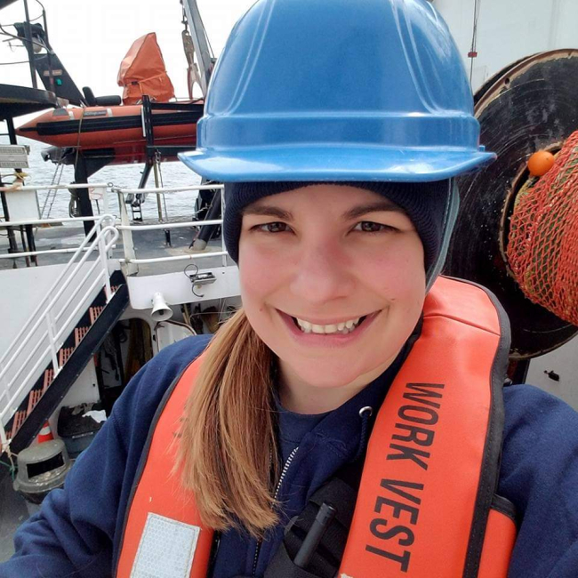 Andrea poses aboard a NOAA vessel and wears a hardhat and work vest.