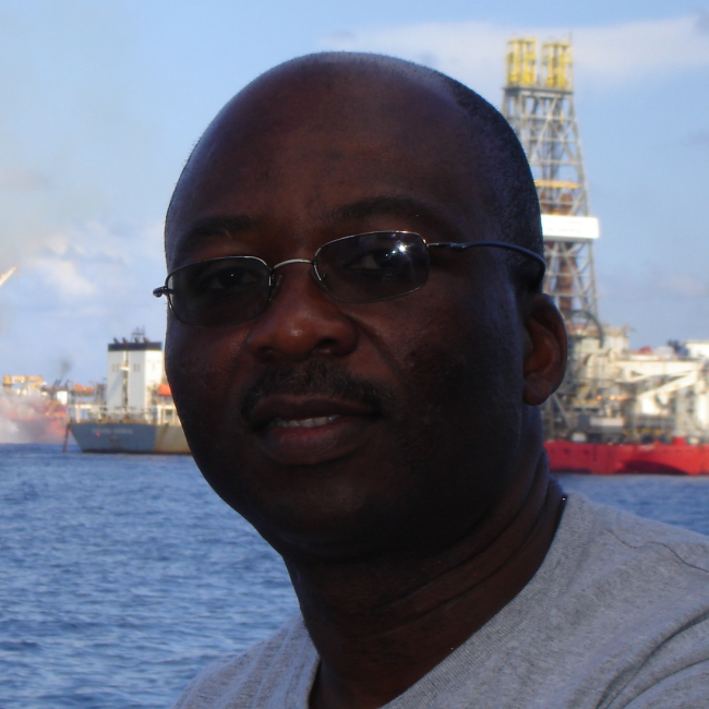A headshot of Dennis in front of large NOAA vessels at sea