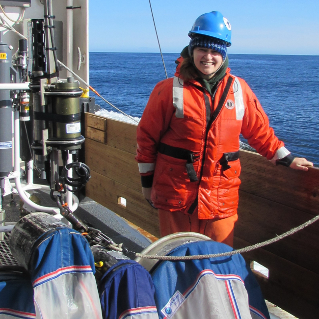 Hollings alumna Hillary Thalmann samples for larval Pacific cod in the Gulf of Alaska on the NOAA ship Oscar Dyson during her 2016 internship. Hillary poses on a ship with larval fish sampling nets and large water-quality samplers. She is wearing cold-weather field field gear and a safety helmet.