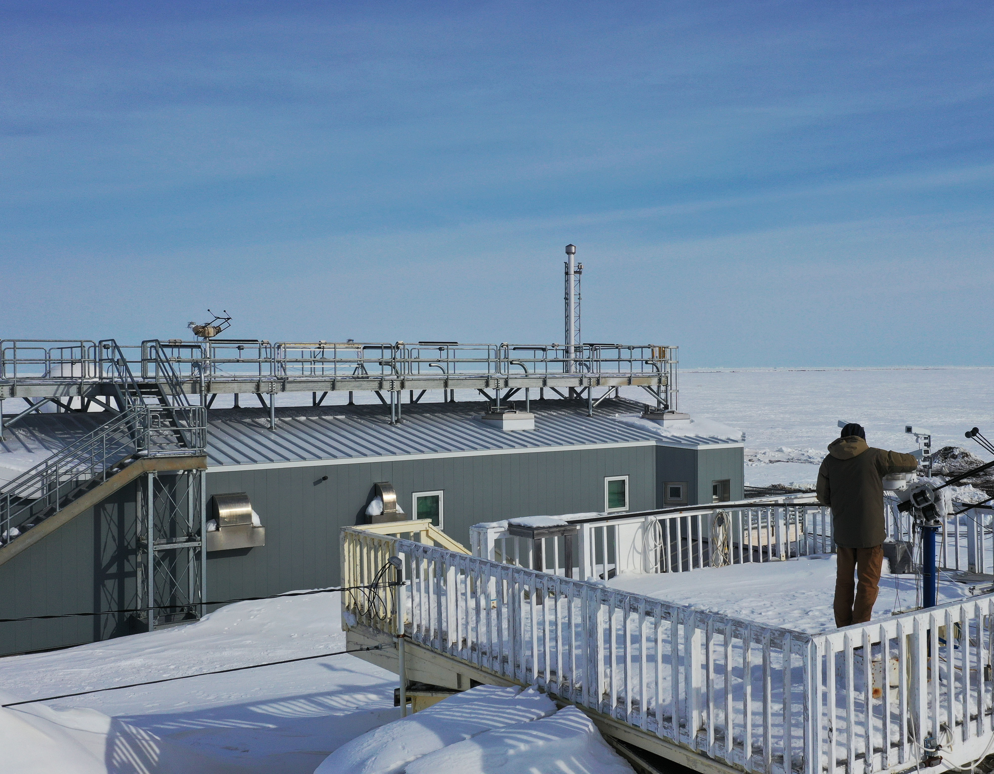 On the old roof, ice is cleared off sensors on instruments that measure solar radiation. These instruments and others that measure sky and land-based radiation have since been installed on the roof of the new laboratory (shown in background).