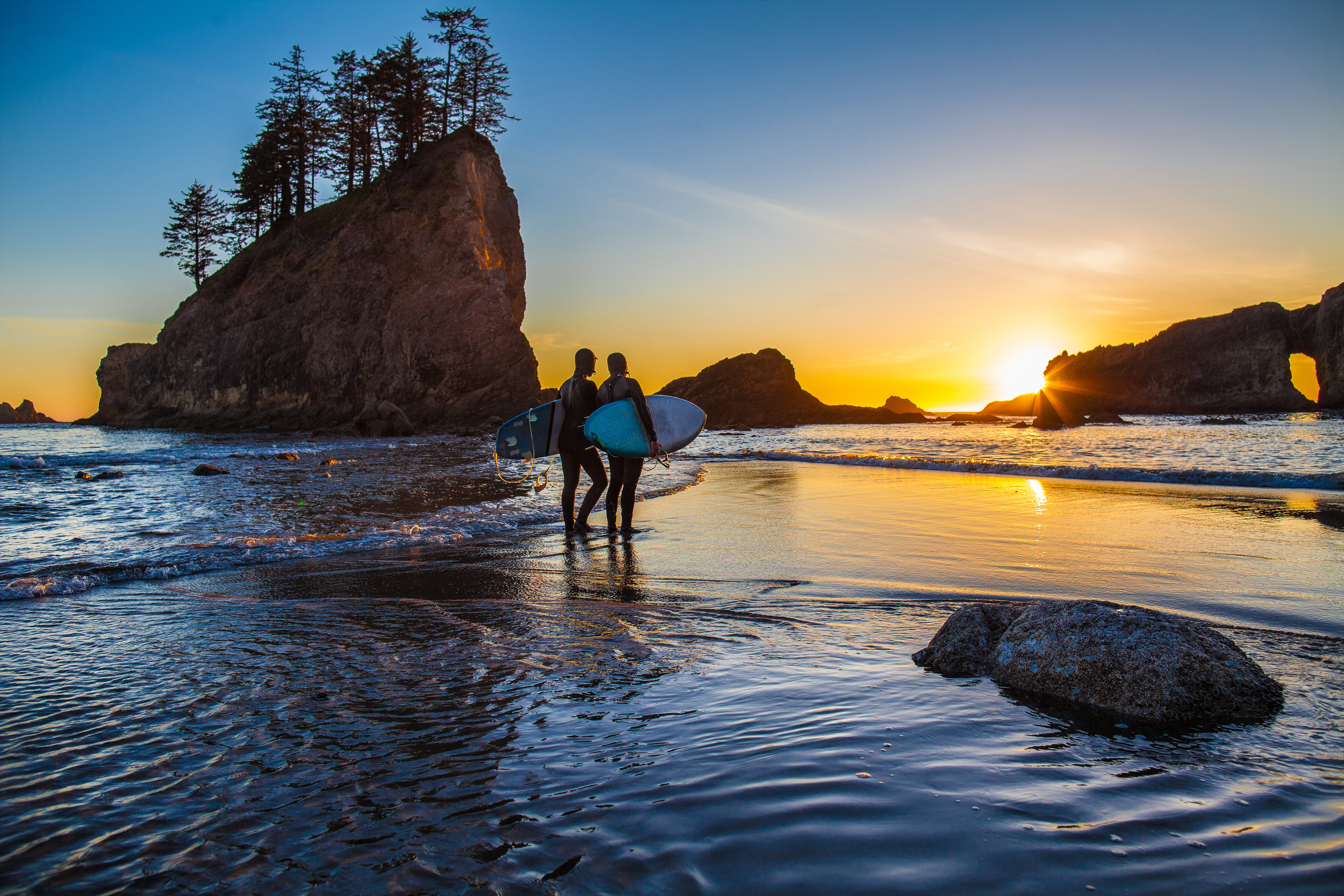 A pair of surfers walk on the shore during sunset in Olympic Coast National Marine Sanctuary