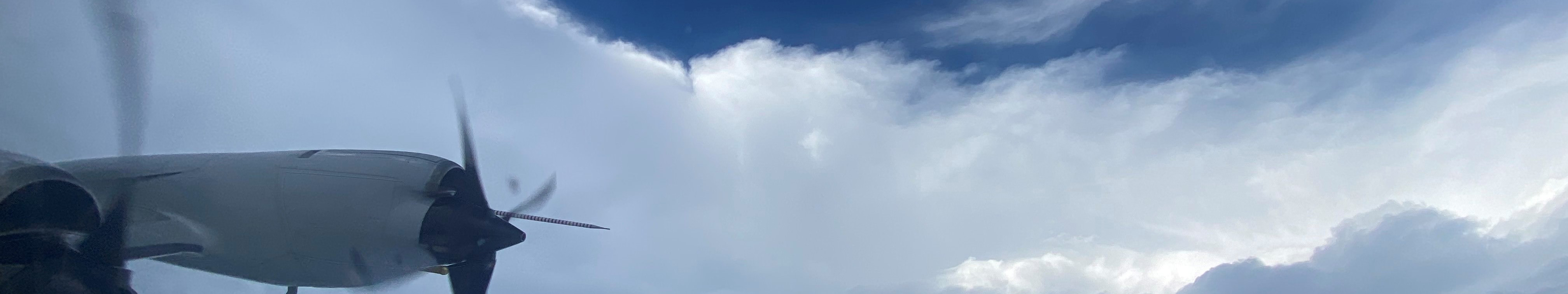 A view of an airplane inside of a hurricane cloud. The curve of the eye wall is visible and there is blue sky above the cloud.