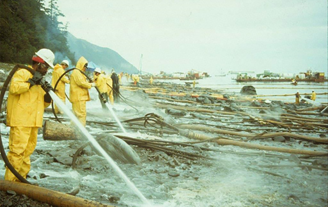 A line of clean-up workers hose off oil from a rocky shore using hot water following the Exxon Valdez oil spill. Exxon Valdez Oil Spill Trustee Council

