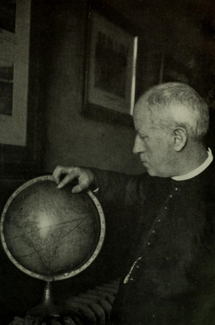 Father José María Algué, inventor of the barocyclonometer, stands looking at a globe and pointing to an area on it.