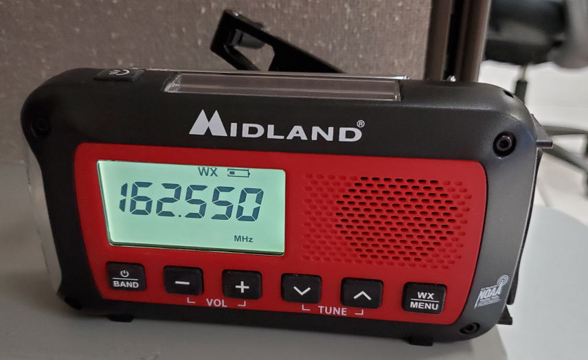 Small black NOAA weather radio made by Midland with red and black housing, an antenna, and six control buttons. 