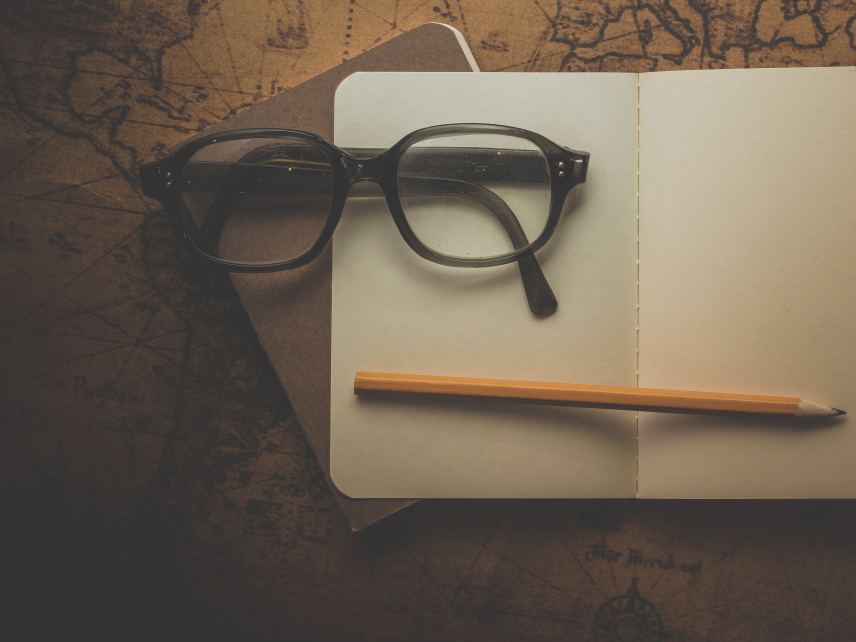 A photo of two field notebooks, a pencil, and glasses sitting on a vintage map.