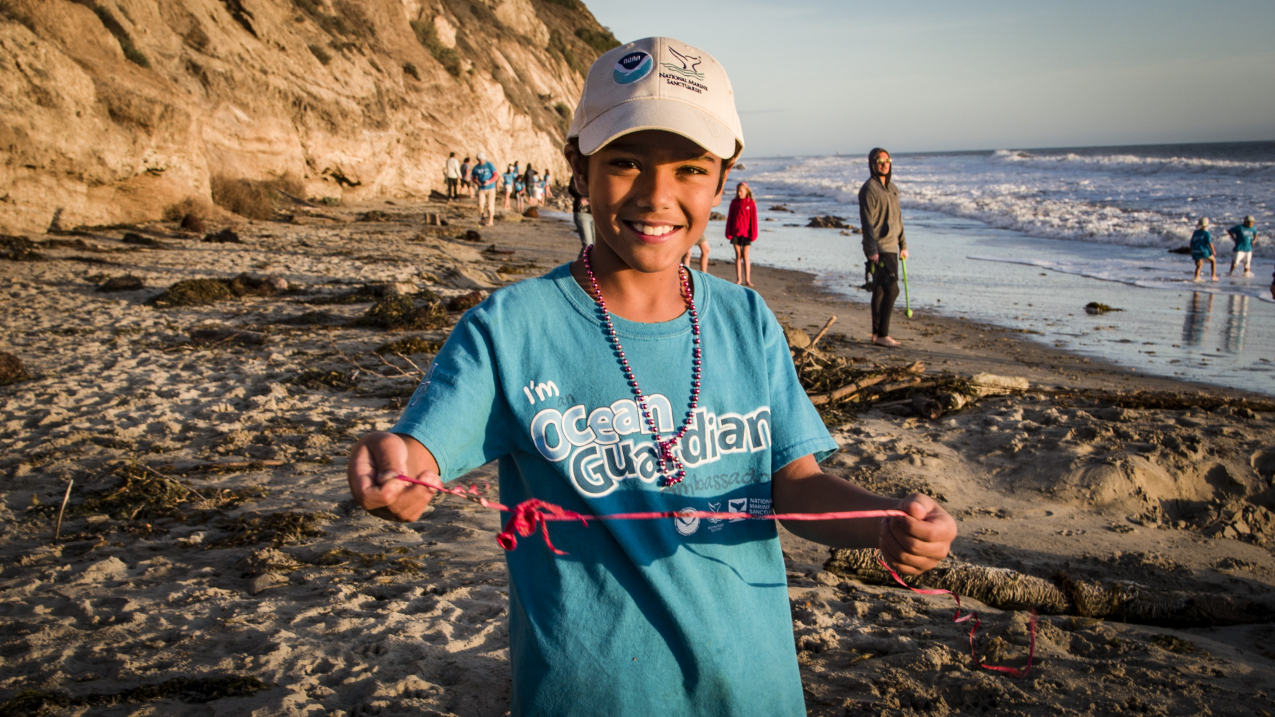 A young student is holding up marine debris from a beach clean up. 