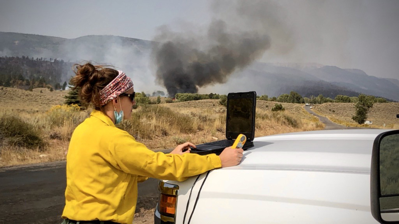 IMET Lisa Kriederman uses a portable weather station to gather observations to support wildfire suppression at the Pine Gulch Fire north of Grand Junction, CO, August 2020. In addition to fire suppression forecasts, IMETs issue timely site-specific forecasts of weather conditions possibly hazardous to crews on the fire line. Weather fronts can change wind speed and direction; dry thunderstorms can cause downbursts, erratic wind conditions and dangerous lightning that can cause additional fires. Wind, humidi