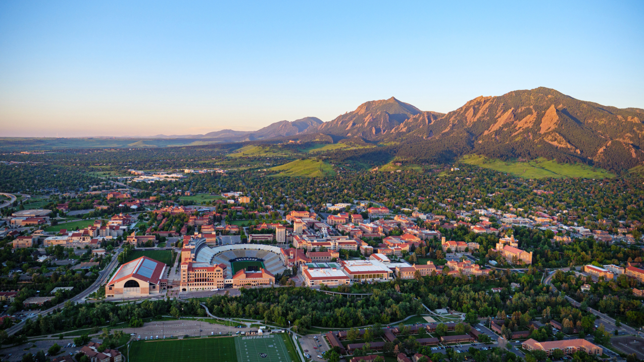 This 2021 aerial photo shows Boulder, Colorado, from the north with the University of Colorado campus in the foreground and the Flatirons in the background. NOAA’s David Skaggs Research Center is located on the Department of Commerce campus, which can be seen at the foot of the grassy hill in the middle of the image.  
