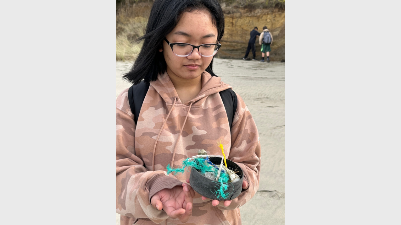 A student looks down at a small pile of marine debris in her hand, including several pieces of frayed plastic lines and numerous small pieces of plastic. Her expression appears to be both sad and disappointed, and she holds one hand palm up in a small shrug.