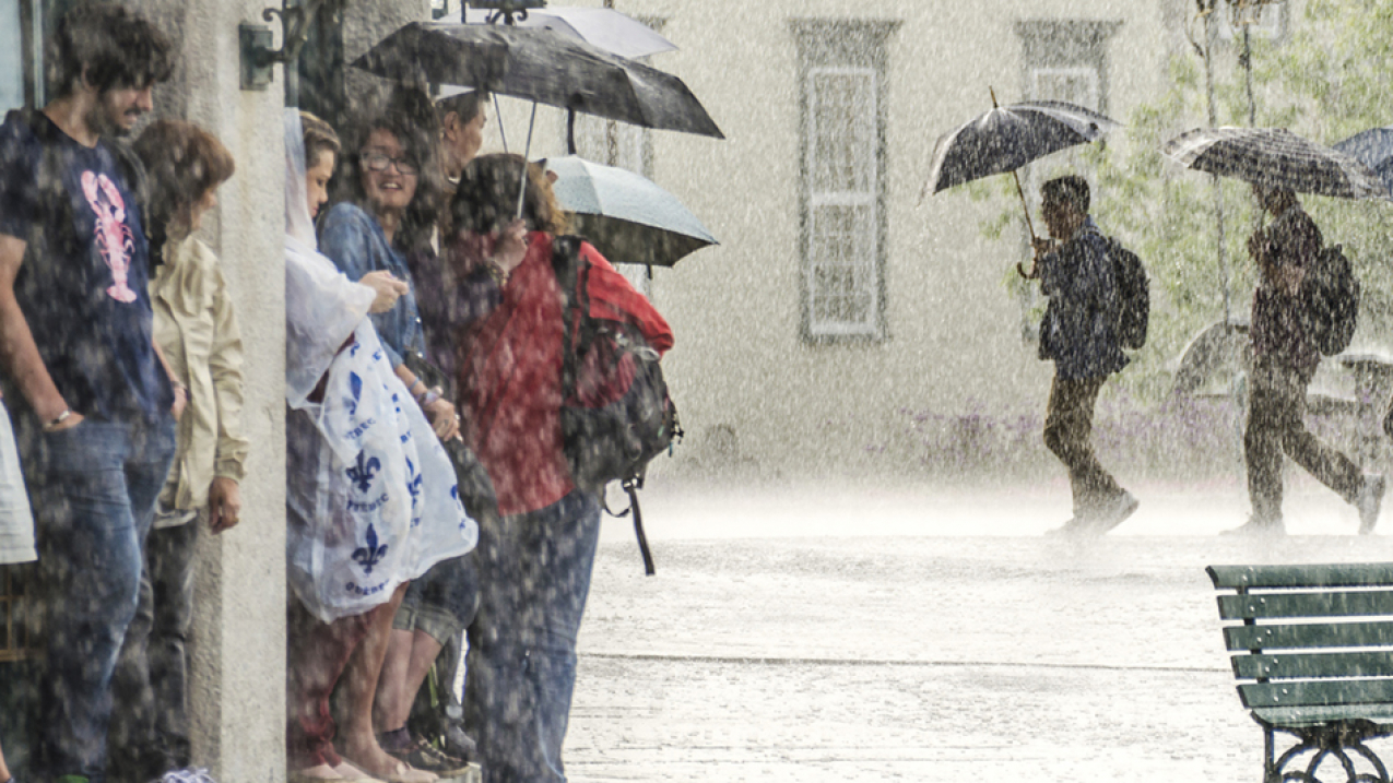 Stock photo of people on the street in Quebec, Canada, taking shelter from a heavy rainstorm, while three people in the background brave the elements with umbrellas.