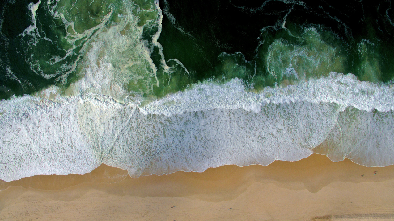Aerial view of waves crashing on a sandy beach.