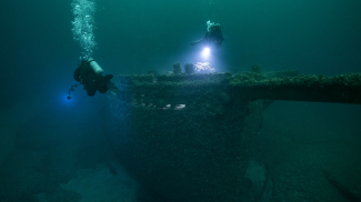 a greenish-blue underwater scene of divers illuminating a shipwreck