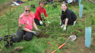 2 students planting trees with an adult during a restoration field trip