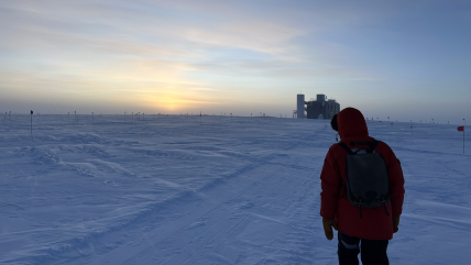 A South Pole station staffer looks west from the main NSF South Pole station toward the IceCube neutrino observatory, as the sun sets over the horizon.