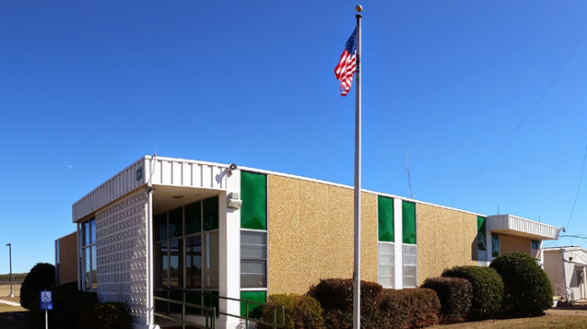 A photo of a low-rise building with a United States flag raised on top of a pole in the front. 