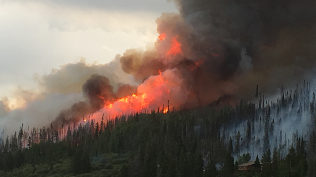 A bright orange wildfire with billowing black smoke looms over the evergreen hills outside Walden, CO.