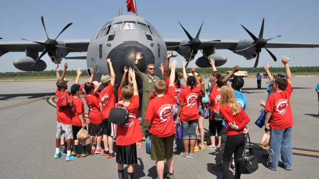 A photo of a pilot talking to a group of elementary students in front of a plane.