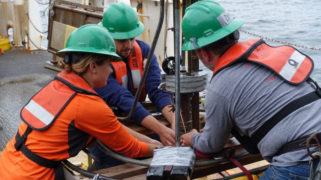 Leslie Irwin (left, NCCOS Silver Spring), Anthony Lima (center, graduate student at University of Texas Rio Grande Valley), and Dave Kidwell (right, NCCOS Silver Spring) carefully remove a core of sediment collected by the Craib corer from the bottom of the Gulf of Maine.