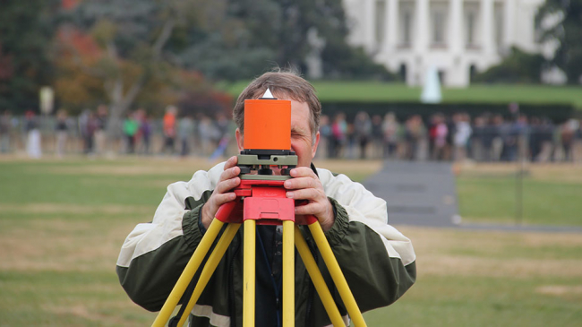 A geodesist on the National Mall looking through a surveying device.