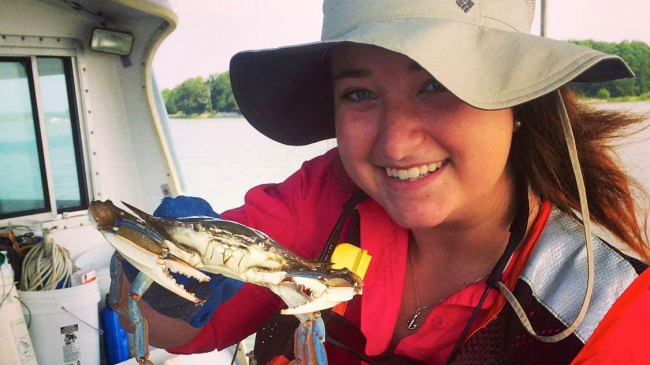 A student is on a research vessel holding a blue crab.