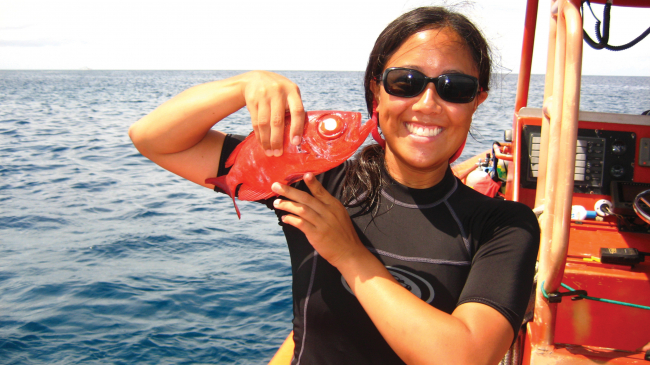 Kimberly Tenggardjaja holds a small red fish onboard a research vessel.
