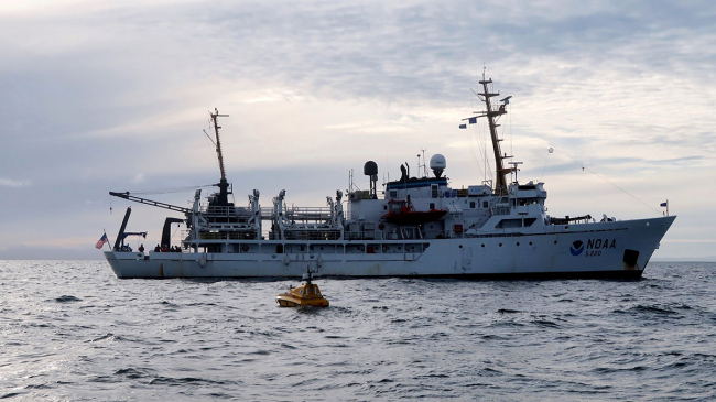 The unmanned surface vehicle BEN ( seen in yellow, bobbing on the ocean surface) launched from NOAA Ship Fairweather in U.S. Arctic waters, July 28, 2018.