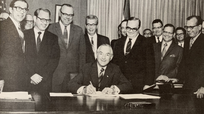 Secretary of Commerce Maurice H. Stans signs the department orders needed to put NOAA in operation on October 3, 1970. Dr. White is standing over Sec. Stans’ left shoulder.