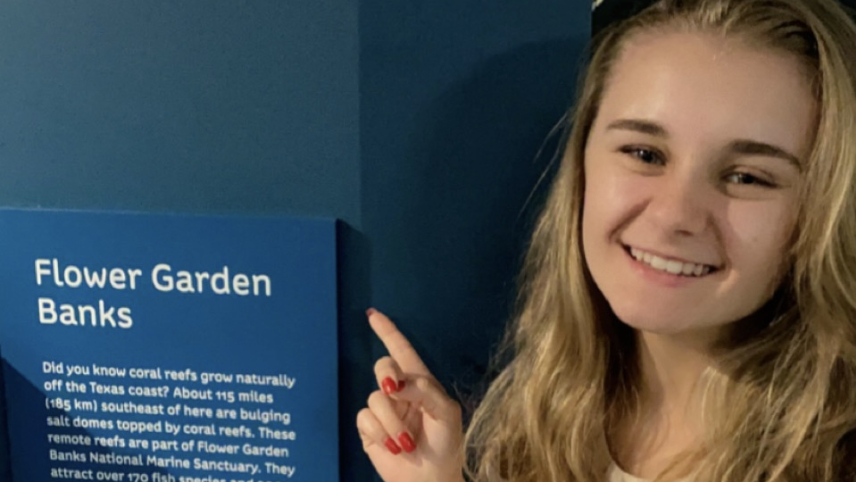 Emily Fritsche pointing to a wall sign that reads, "Flower Garden Banks."