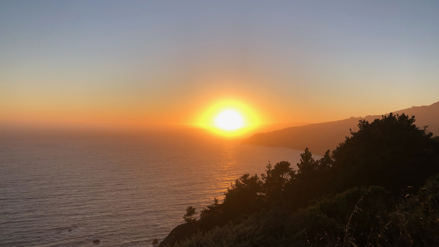 A sunset looking over forested headlands and the Pacific Ocean. 
