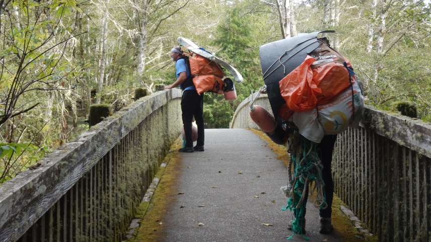 Volunteers carrying large loads of marine debris take a break along a bridge overlooking the Ozette River in Olympic National Park to enjoy the beauty of the fall foliage.