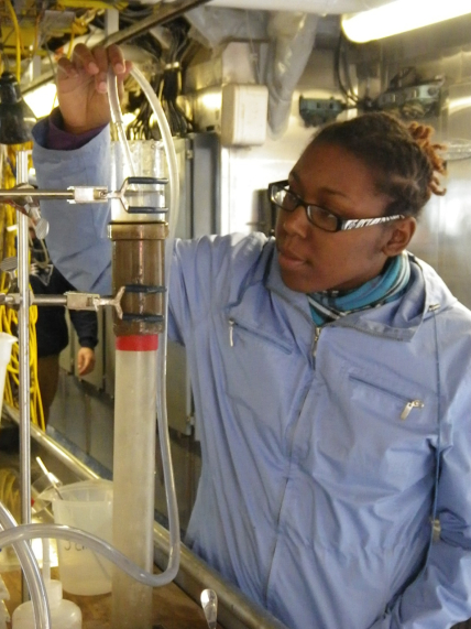  Shareena holds a clear tube at the top of a graduated cylinder to syphon water to collect samples.