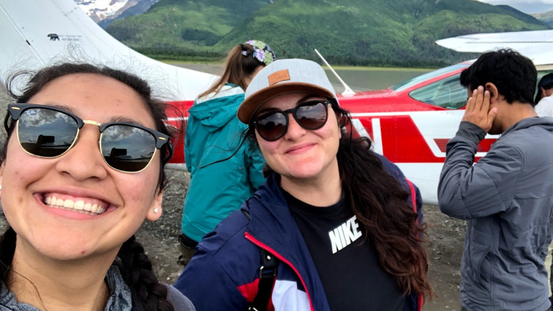2018 NOAA Educational Partnership Program with Minority Serving Institutions (EPP/MSI) undergraduate scholars Analyssa Hernandez (left) and Annalise Guthrie (right) standing in front of a small plane at their internship field site at the Kachemak Bay National Estuarine Research Reserve in Homer, Alaska.