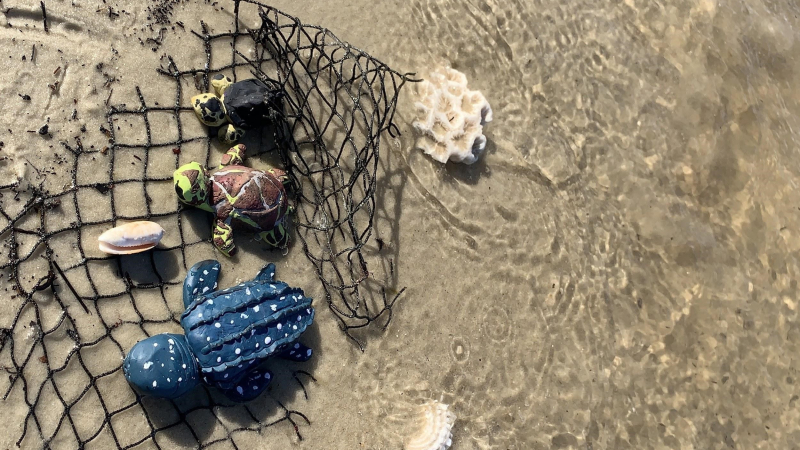 Child’s sculptured sea turtles caught in a net on a sandy beach.