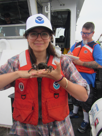 Barbara Bevacqua, a 2018 NOAA Hollings scholar, stands on the research vessel Victor Loosanoff while holding a spider crab that was found in an oyster cage. Research was completed in Long Island Sound, roughly off of Westport, Connecticut. Fish biologist/taxonomist Paul Clark and NOAA Corps Captain, Lt. Erik Estela are in the background, to the right and left, respectively.