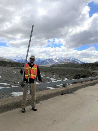 True Furrh holds a river gauge over the Toklat East Fork in Denali National Park, with the Alaska Range in the background. Furrh completed his Hollings scholar internship in Summer 2019.