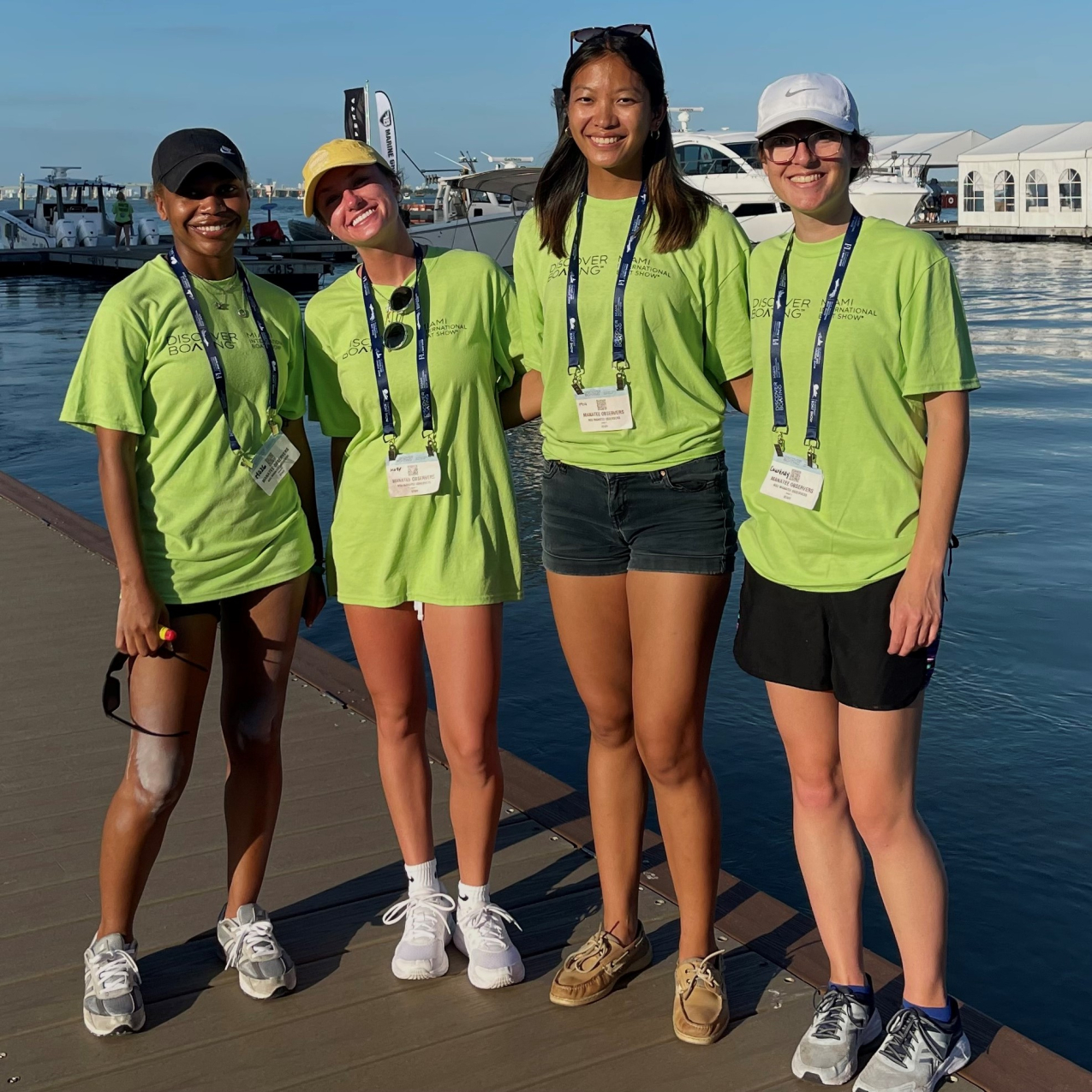 Four people pose together on a pier. They wear bright yellow shirts that say “Discover Boating, Miami International Boat Show” and have lanyards identifying them as manatee observers.