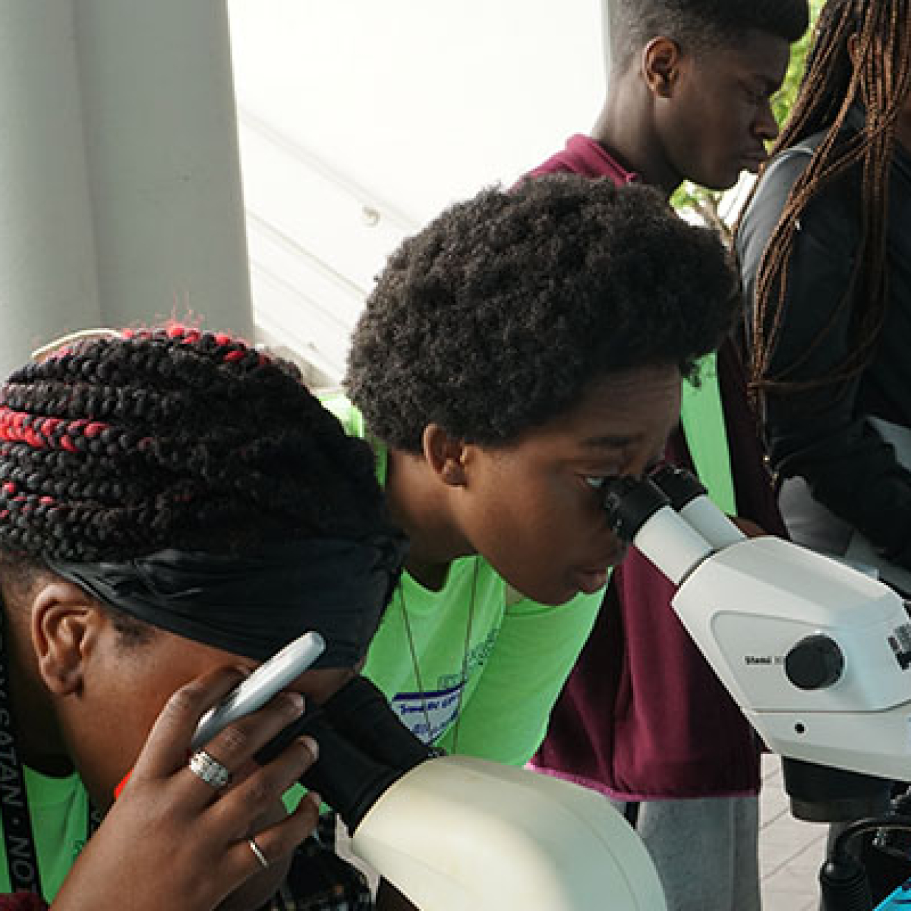 Two high school students look into microscopes.