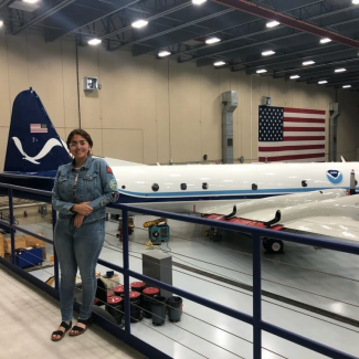 Nohemi poses in a large garage with a plane that has a NOAA Logo