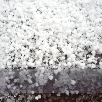 Appears to be irregular spheres of snow, each smaller than about five millimeters. The pellets look soft to the touch and below the top layer, they look to be melting into an icy slush.