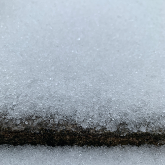 A close up of sleet on concrete. The sleet is made up of irregular translucent ice spheres that are of varying sizes, but all smaller than a few millimeters in diameter.