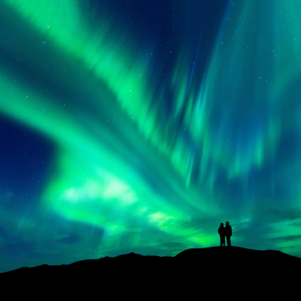 Aurora borealis with silhouette of couple on the mountain.