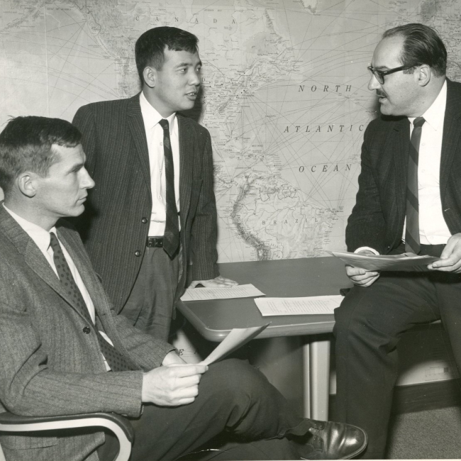 A black and white photo shows Joseph Smagorinsky, Kirk Bryan, and Suki Manabe sitting and discussing a paper in 1969.